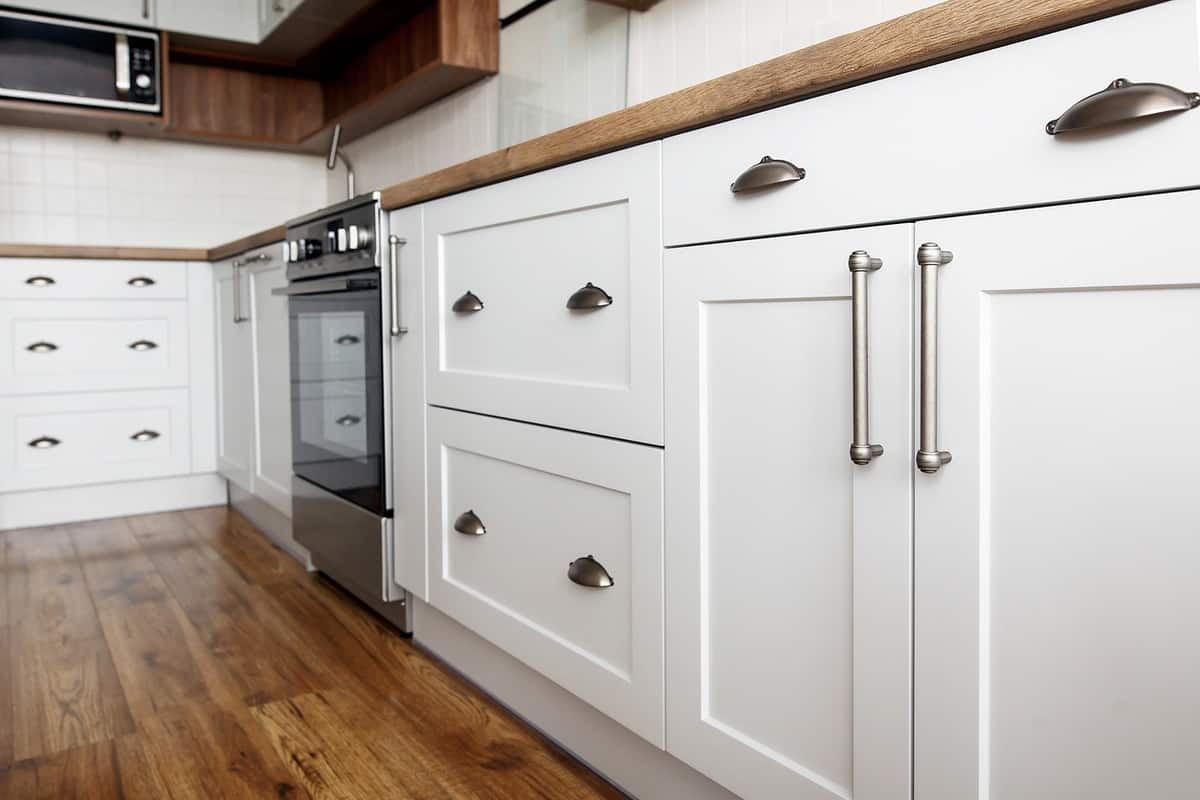 White Kitchen Cabinets Refinishing Bright white painted kitchen cabinets with shaker-style doors, stainless steel hardware, and dark wood countertop in modern
