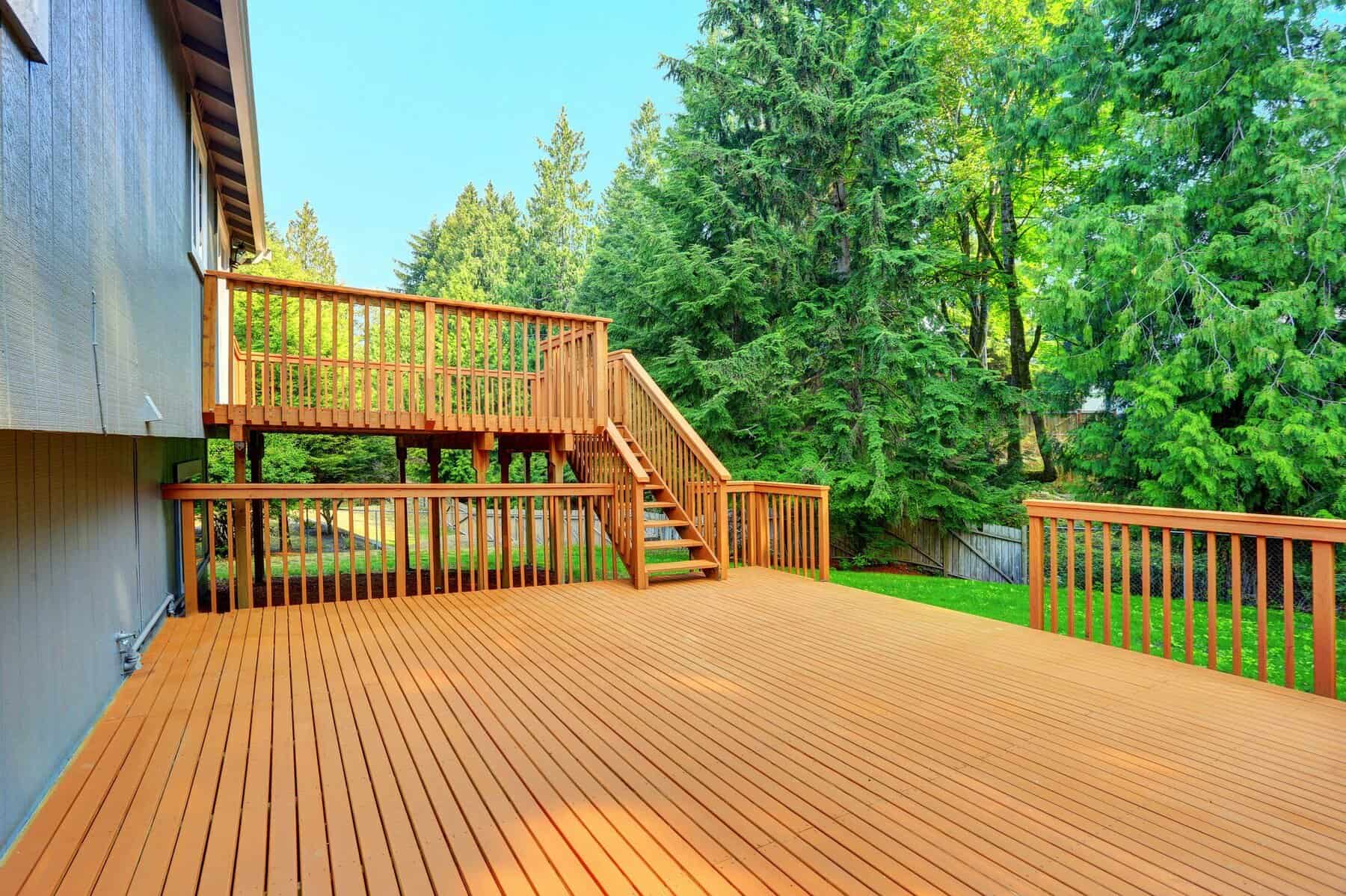 Cedar Stained Residential Deck Cedar-stained wooden deck with matching railings and stairs adjoining residential home surrounded by trees