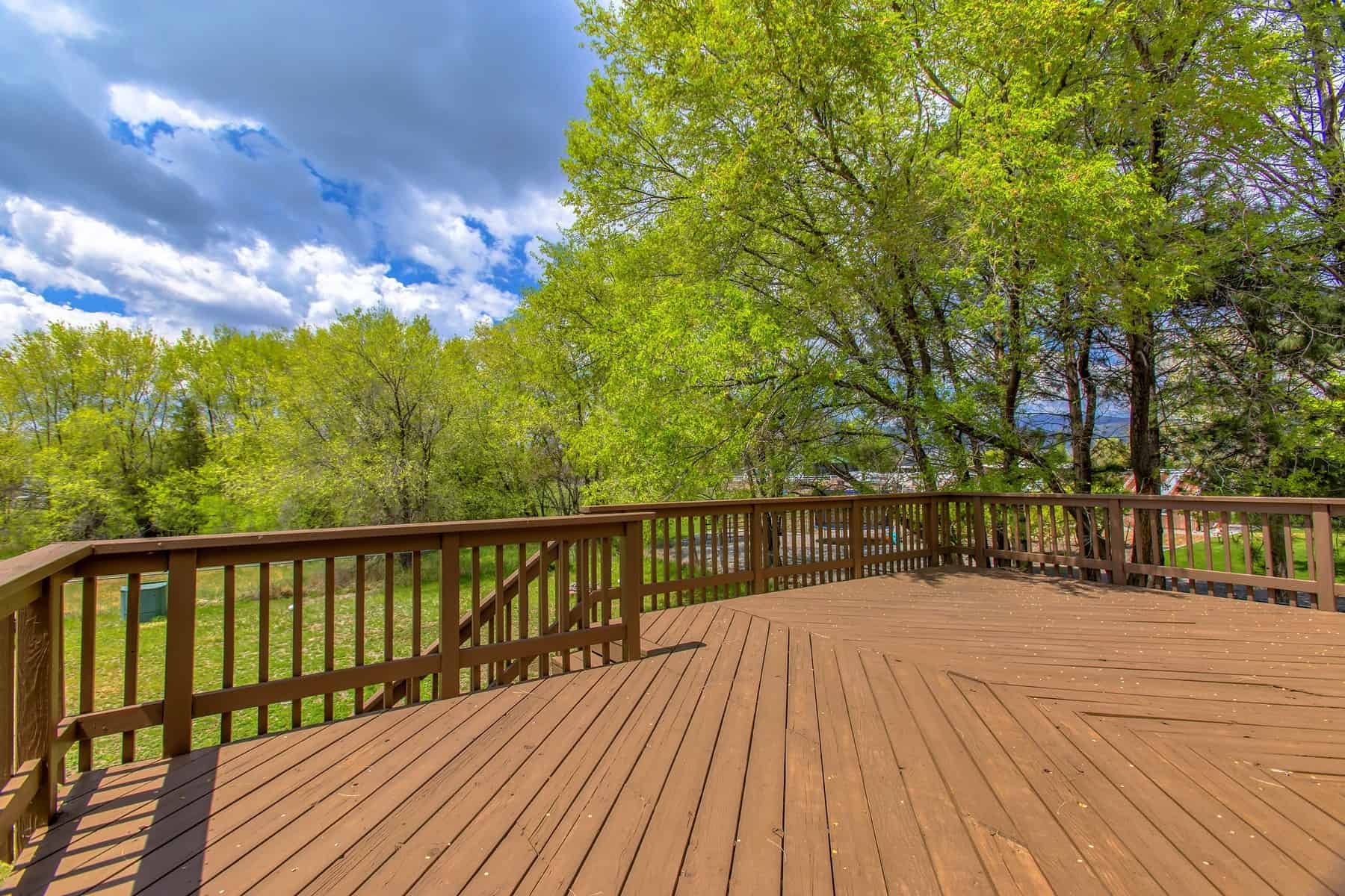Medium Brown Stained Wooden Deck Medium brown stained wooden deck with matching railings overlooking green trees in Raleigh, NC
