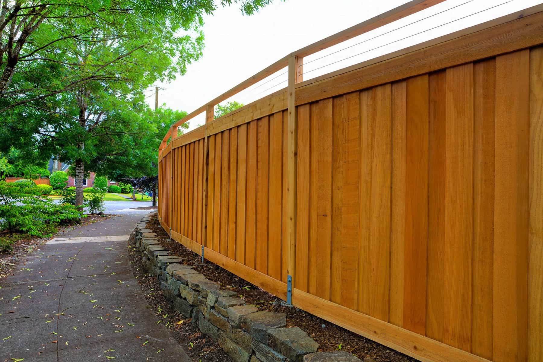 Cedar Stained Wooden Fence Cedar-stained wooden fence with vertical board siding and white vinyl top rail along residential pathway in Raleigh, NC