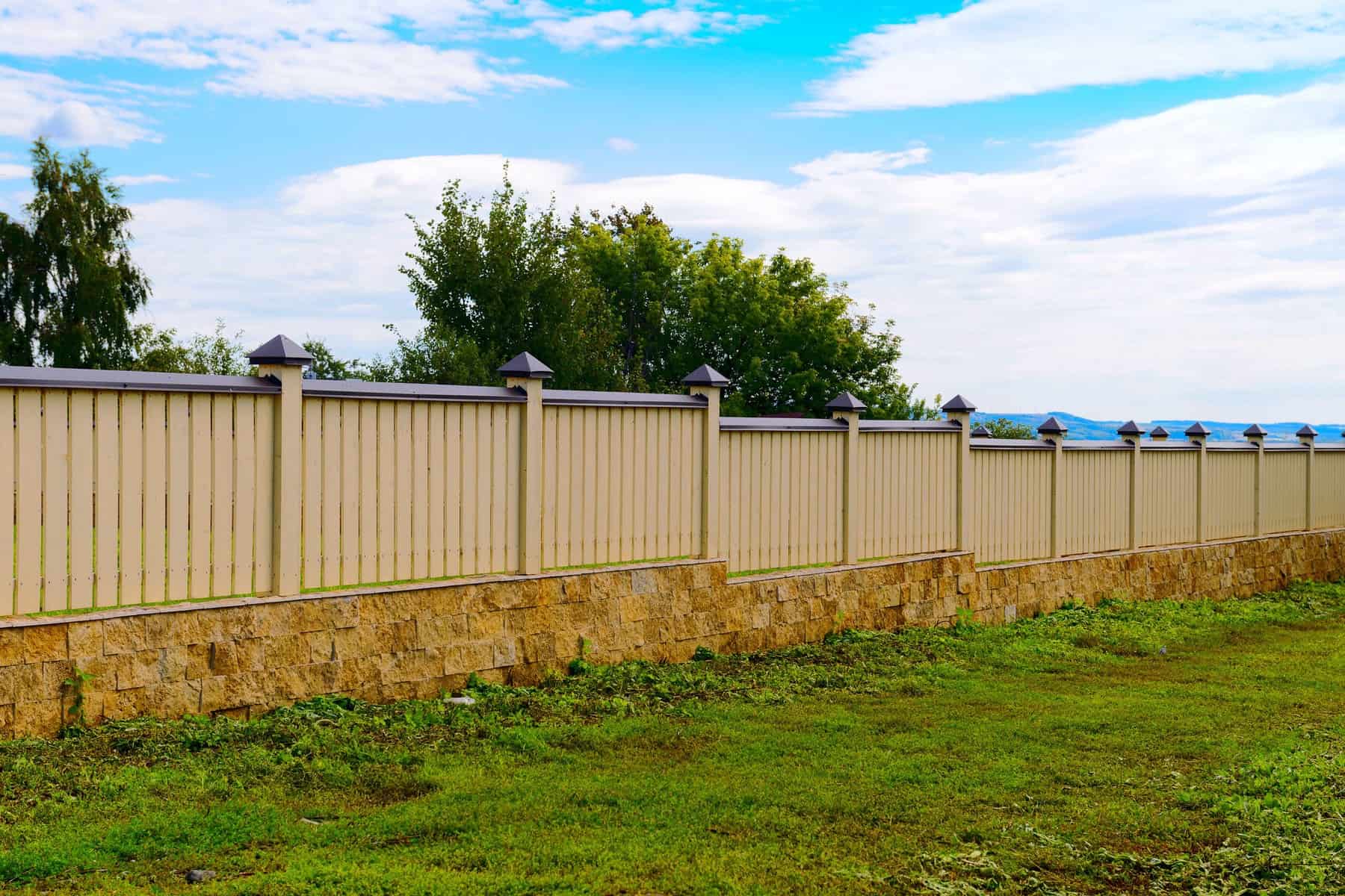 Tan Metal Fence Panels Tan corrugated metal fence panels with black posts and stone base in residential setting
