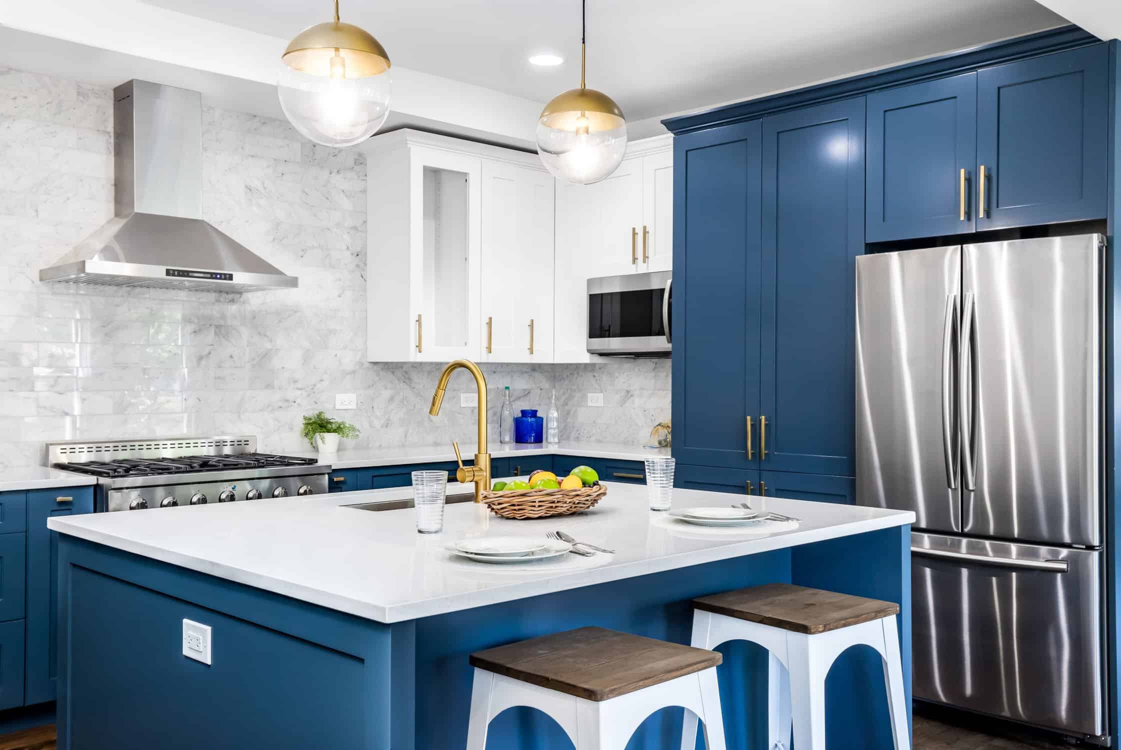 Navy Blue Kitchen Cabinetry Navy blue painted kitchen cabinetry with white upper cabinets, white marble backsplash, stainless steel appliances, and