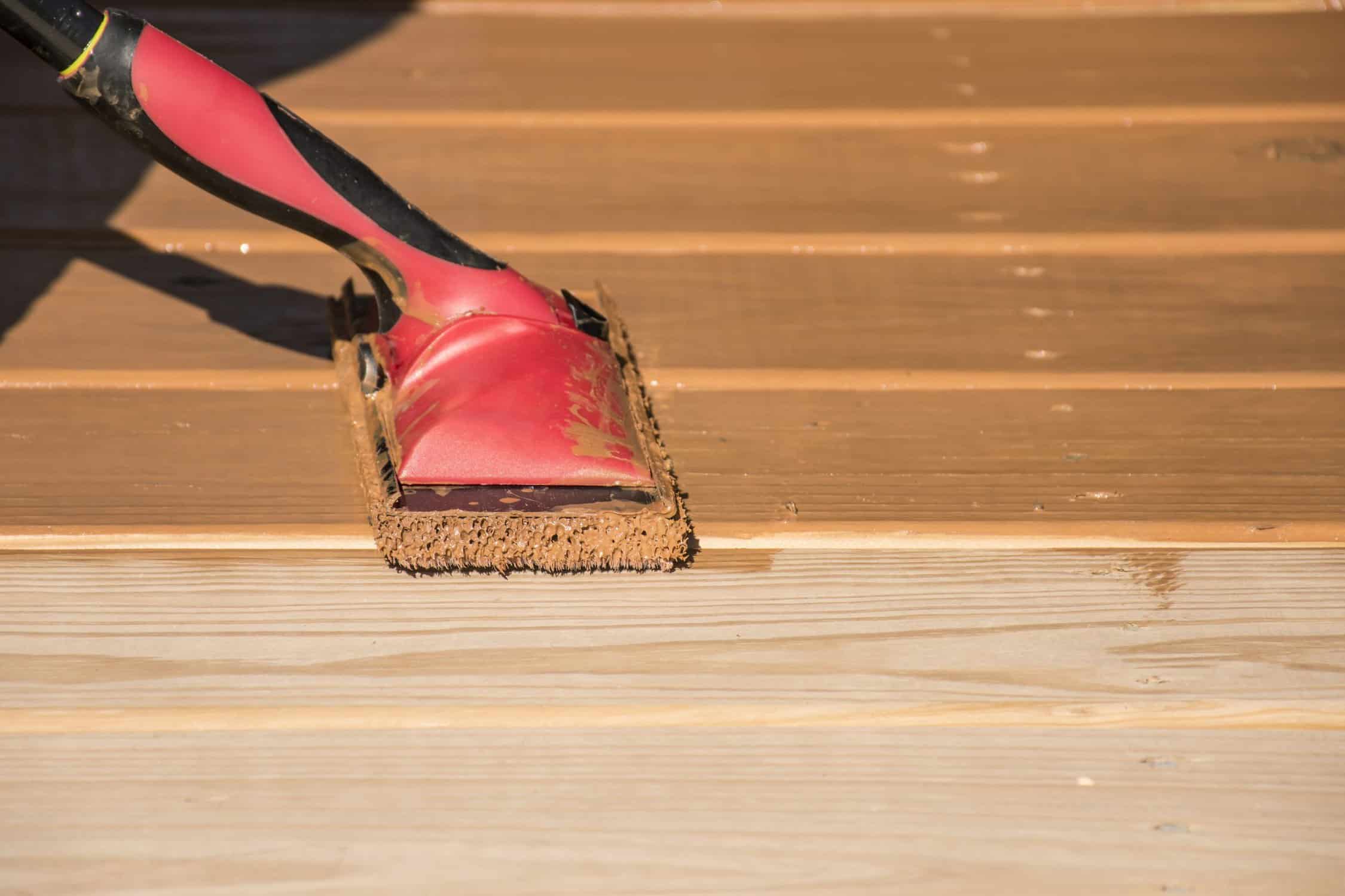 Red Deck Stain Application Red deck stain being applied to light wood decking with natural bristle brush in residential setting