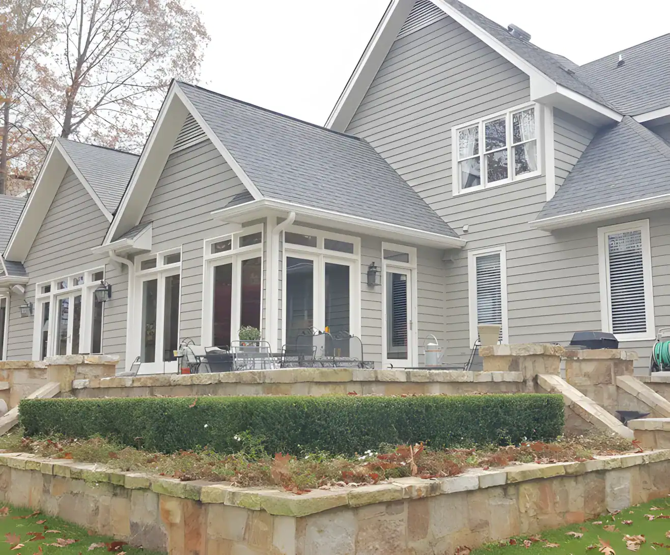 Light gray horizontal-siding two-story residential home with white trim, white multi-pane windows, gray roof, and stone