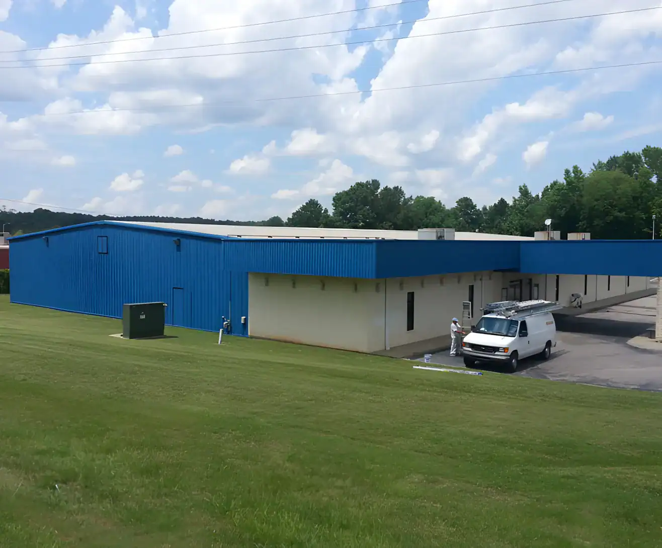 Blue Metal Commercial Building Exterior Bright blue corrugated metal commercial building with cream-painted concrete block lower section and white service vehicle