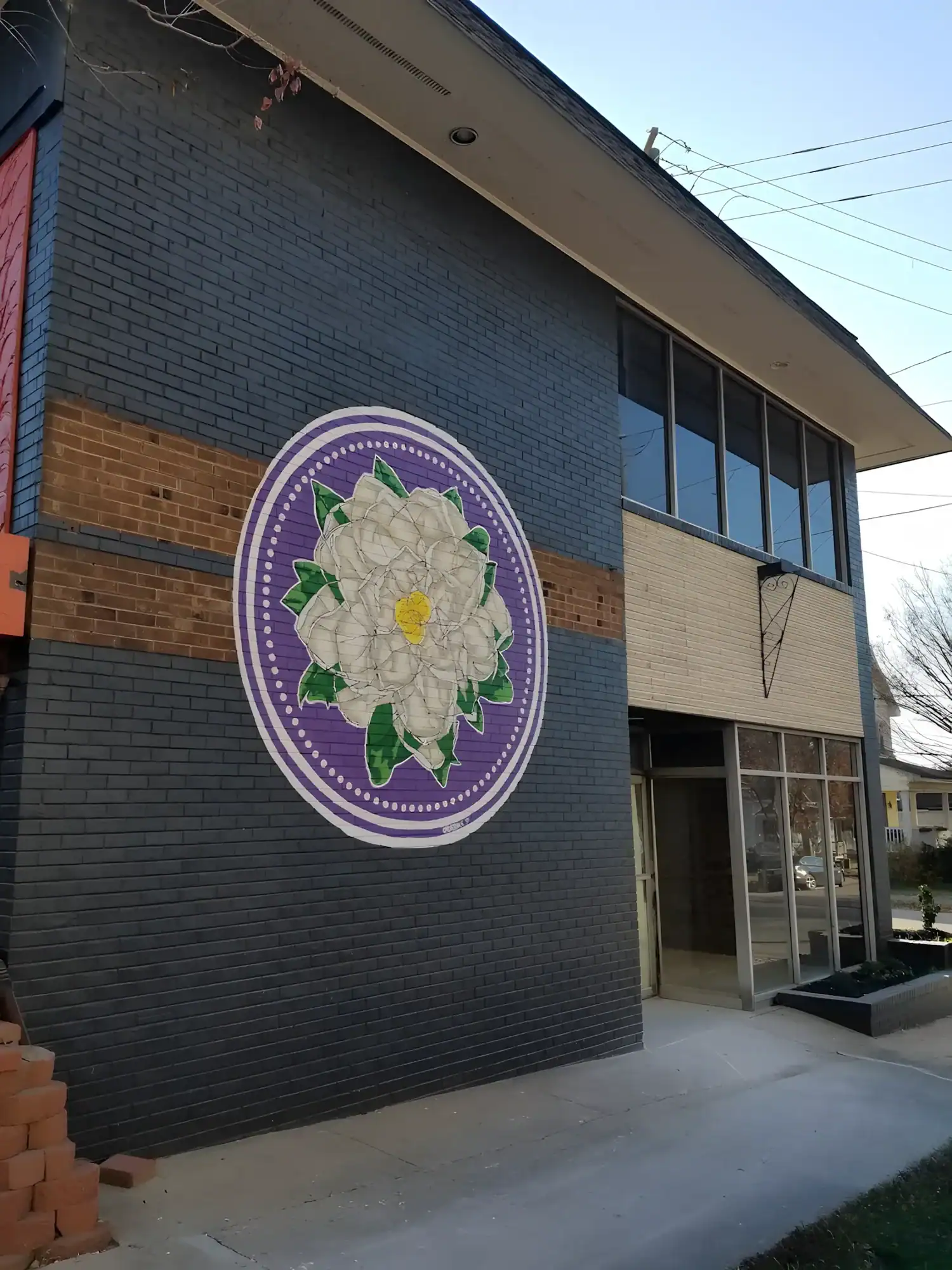 Purple White Flower Commercial Mural Dark gray-painted commercial building exterior with large purple circular mural featuring white flower and green leaves