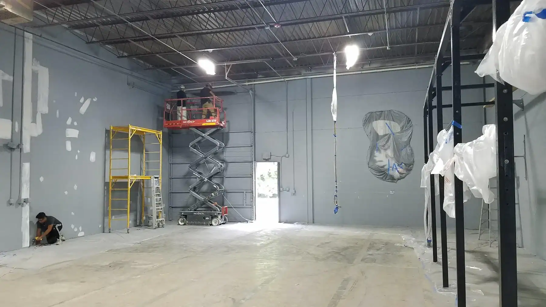 Commercial Interior Painting Project Light gray-painted commercial interior space with concrete floor, industrial ceiling, and construction equipment during
