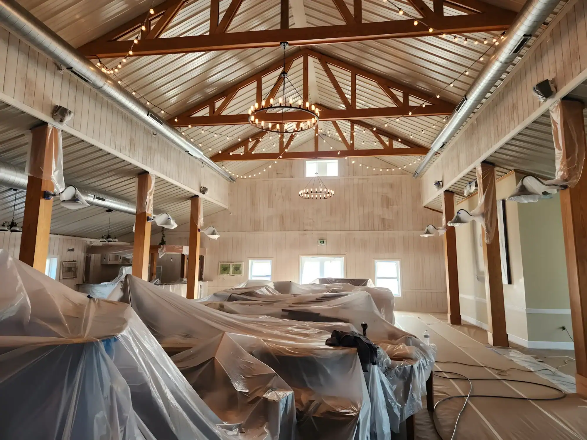 Large Commercial Space Interior Painting Light wood-paneled commercial interior with exposed beam ceiling, protective coverings, and industrial lighting during