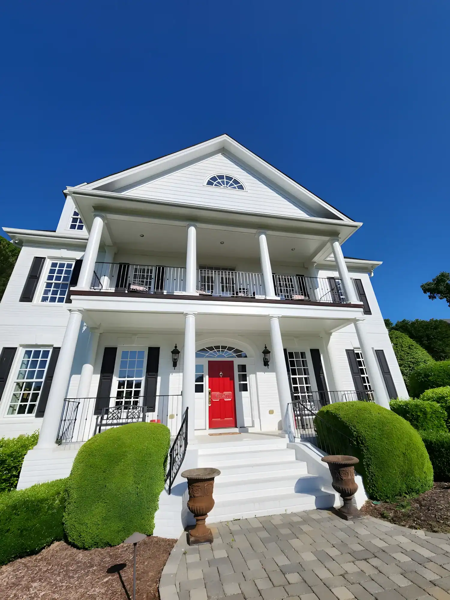 White Colonial Home Exterior White-painted two-story colonial residential home with red entry door, white columns, black trim, and blue clear sky