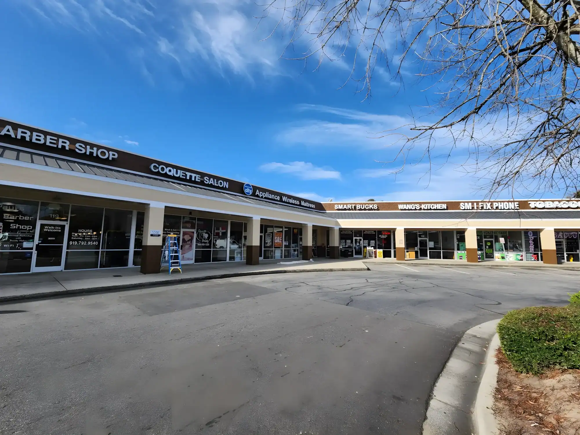 Cream Painted Commercial Strip Mall Cream-painted commercial strip mall storefront with black signage, multiple shop windows, and asphalt parking lot