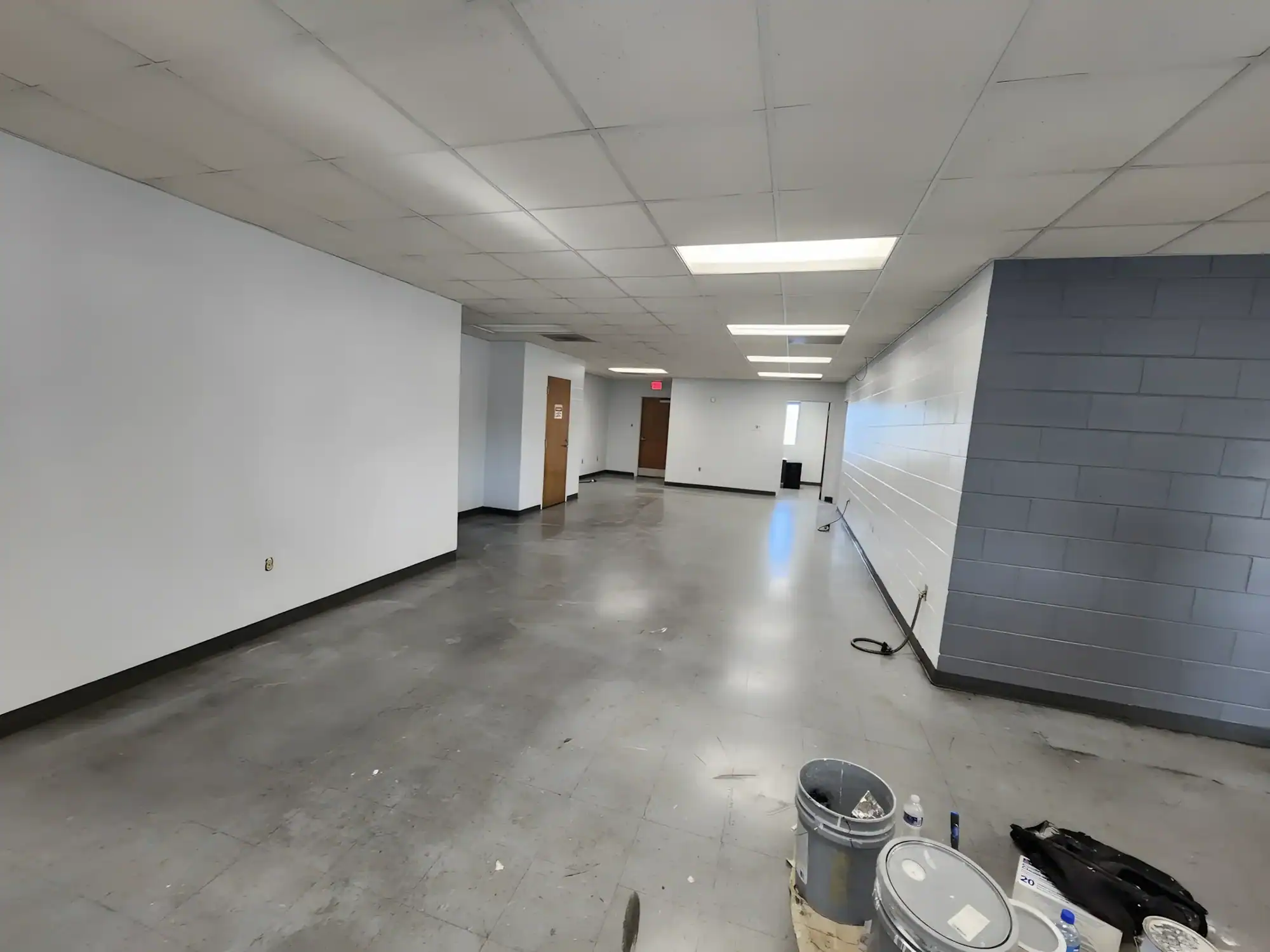 Commercial Interior Space Painting White-painted commercial interior space with concrete floor, drop cloths, paint buckets, and industrial ceiling lighting.