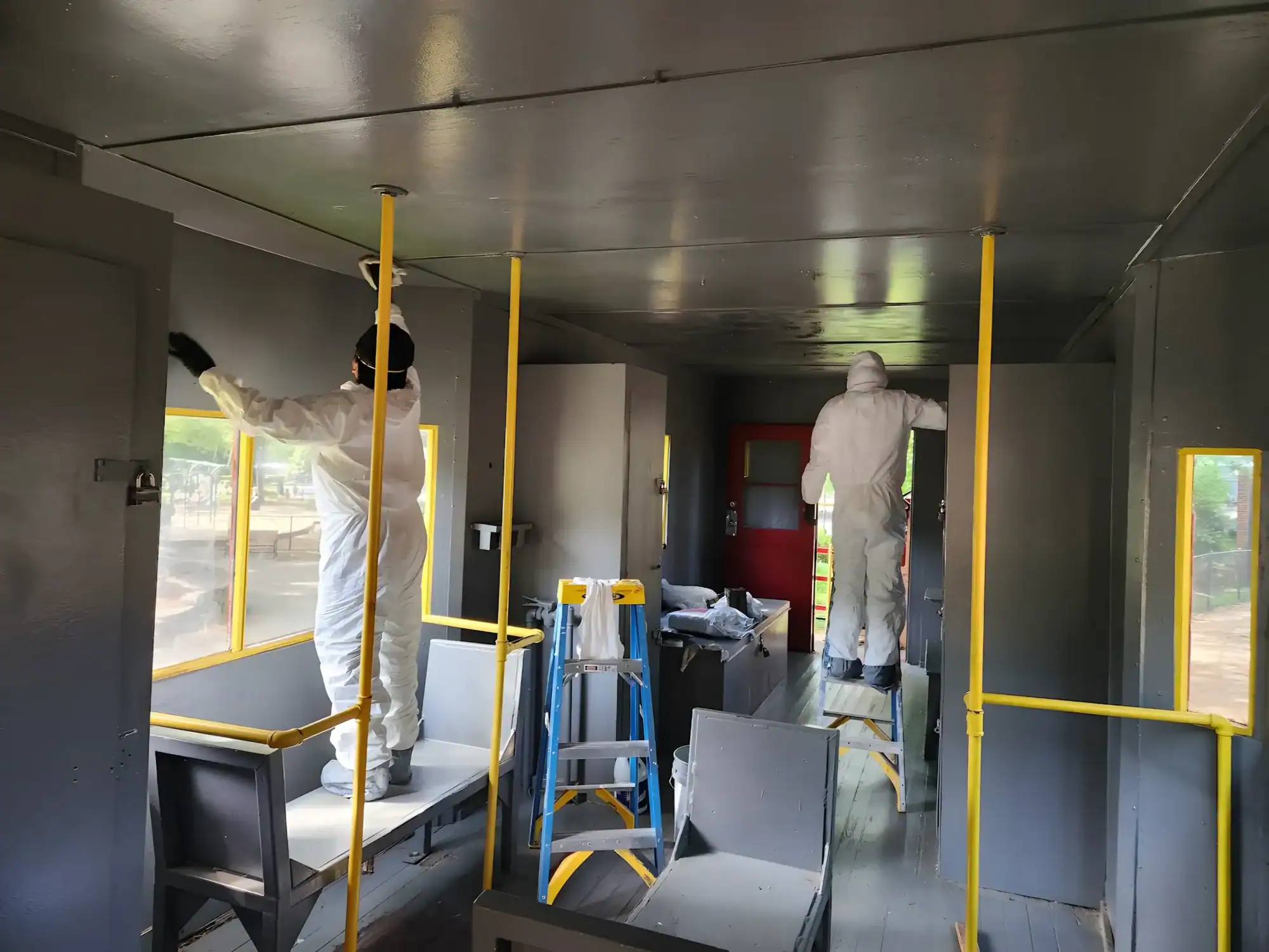Interior Commercial Space Painting Gray-painted commercial interior with metal ceiling, yellow safety railings, and painters in protective suits during