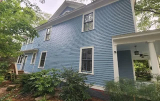 Light blue horizontal-siding two-story residential home with white trim, white-framed windows, and covered entry porch in