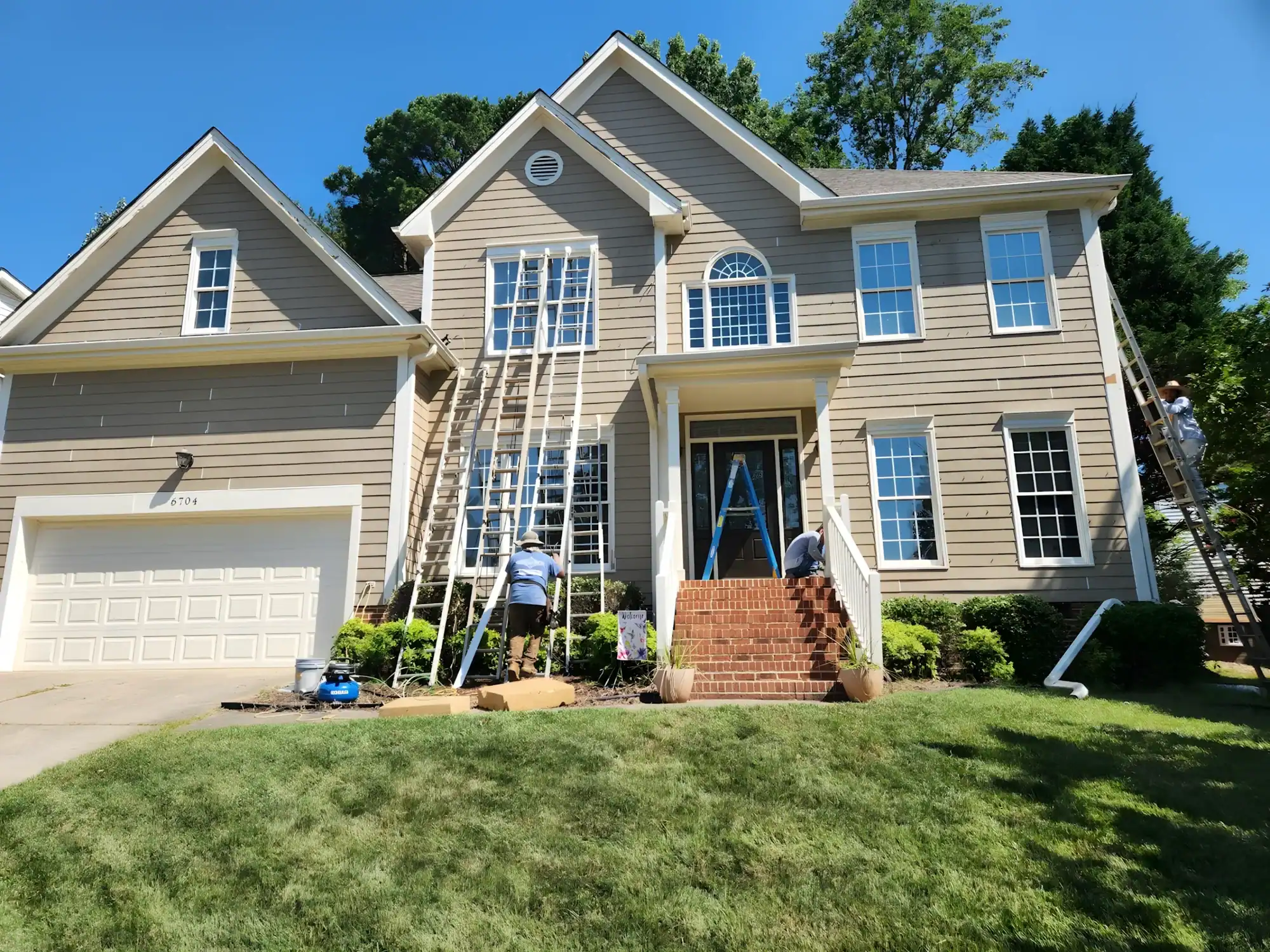 Beige horizontal-siding two-story residential home with white trim, brick front porch, and white garage door in Raleigh, NC
