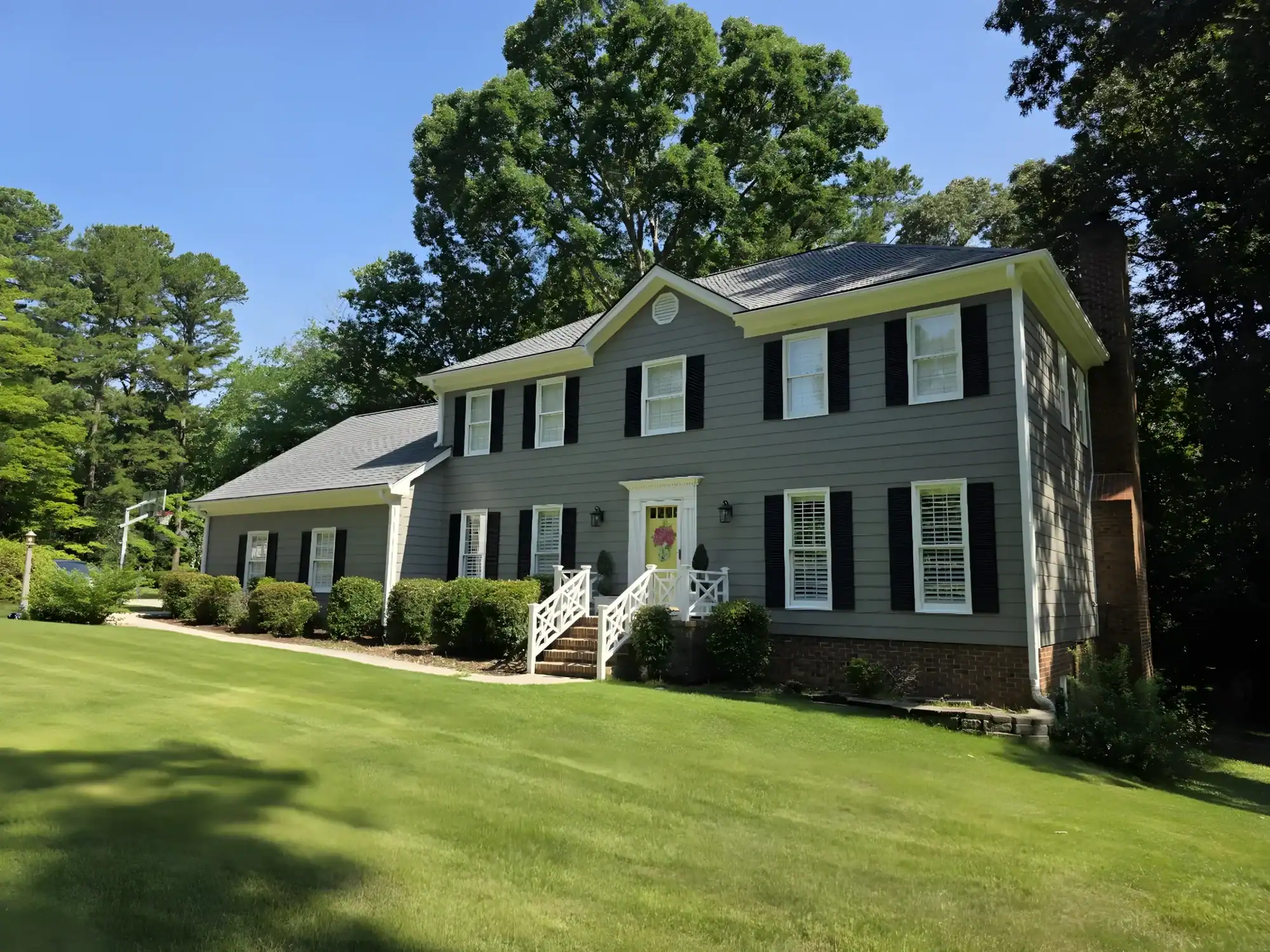 Slate gray two-story colonial residential home with white trim, black shutters, and brick foundation in Raleigh, NC