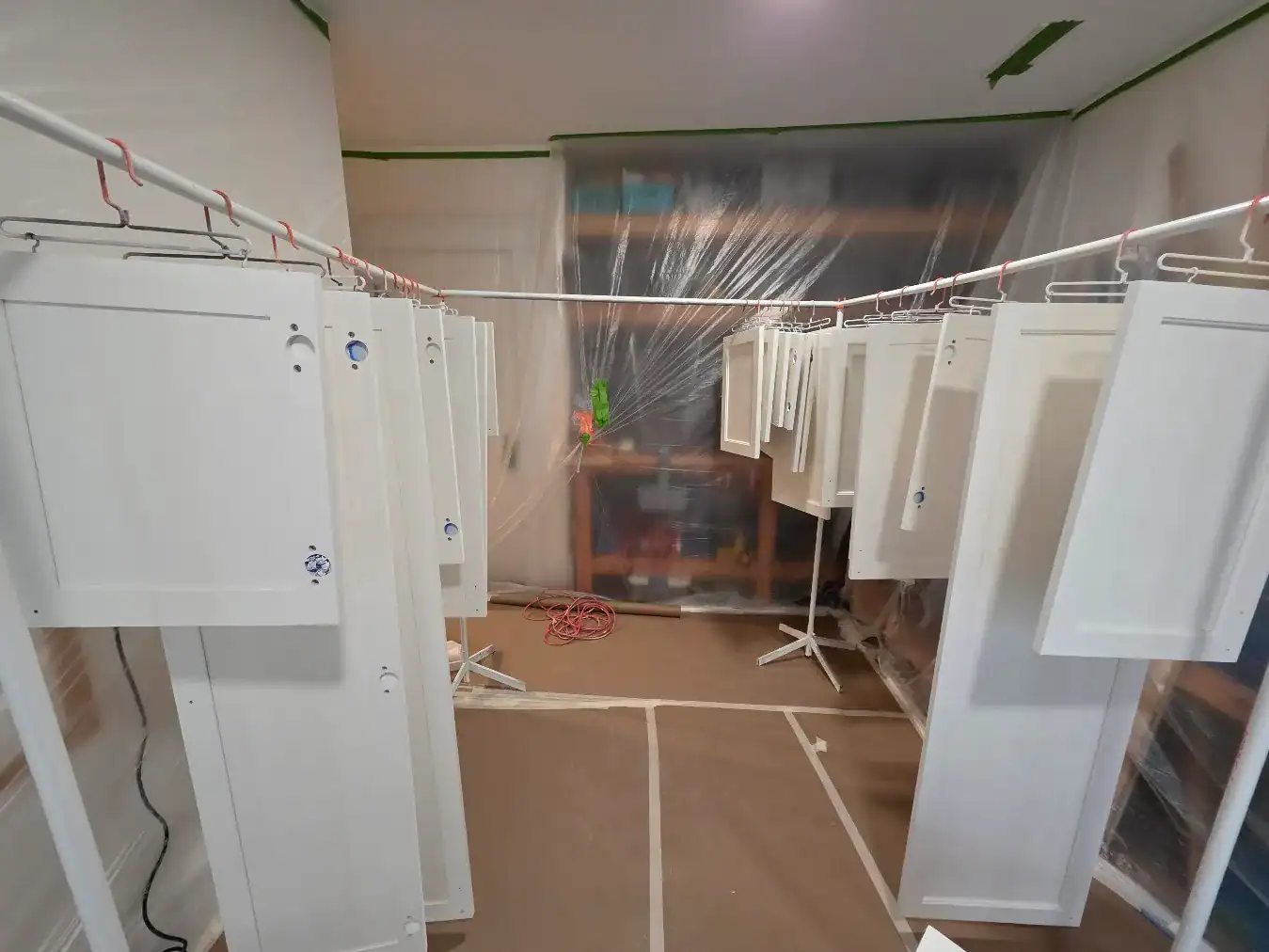 White Painted Cabinet Doors Drying White-painted cabinet doors hanging on drying racks with protective floor coverings in interior workspace