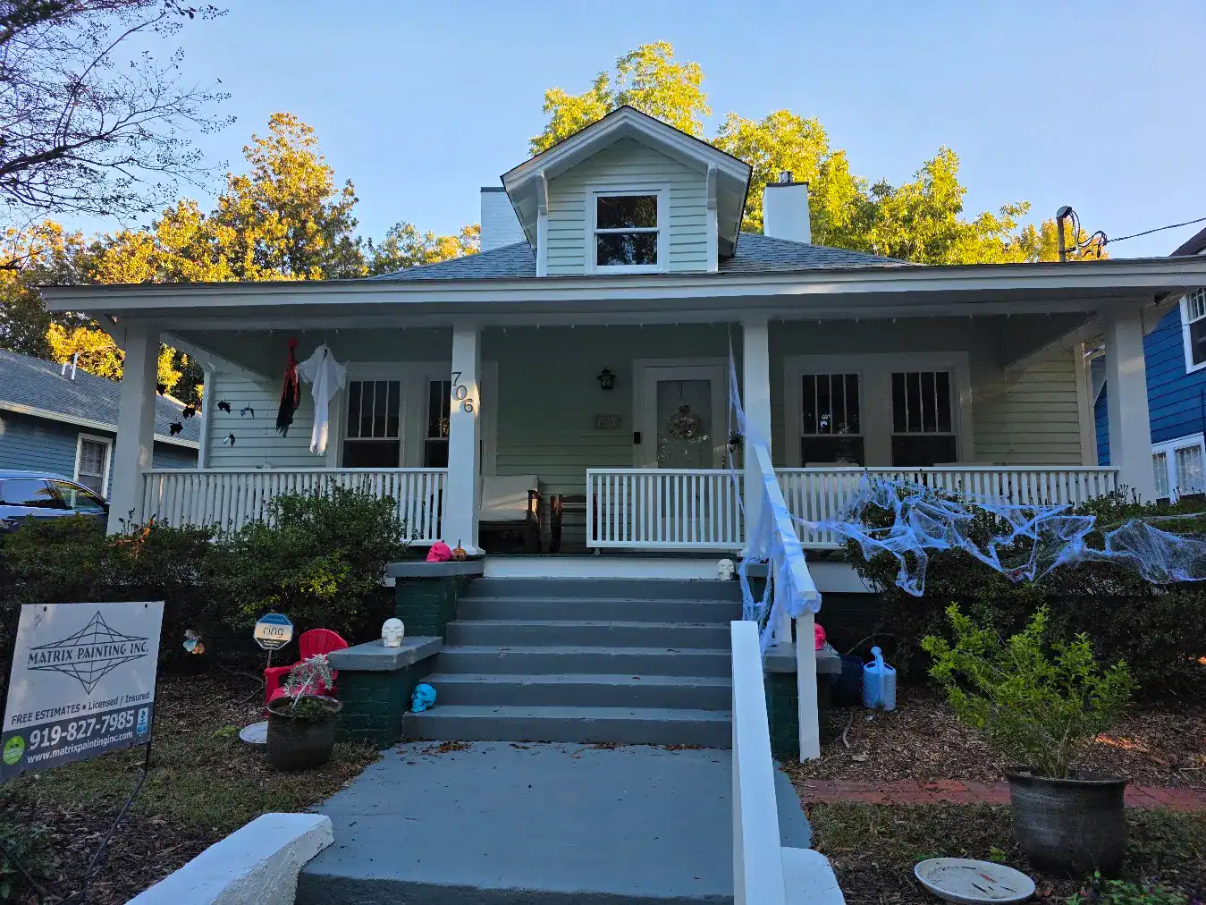 Sage green horizontal-siding single-story residential home with white porch columns, railings, and gable dormer in Raleigh