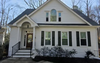 White-painted two-story colonial residential home with black shutters, black roof, white trim, and brick foundation in