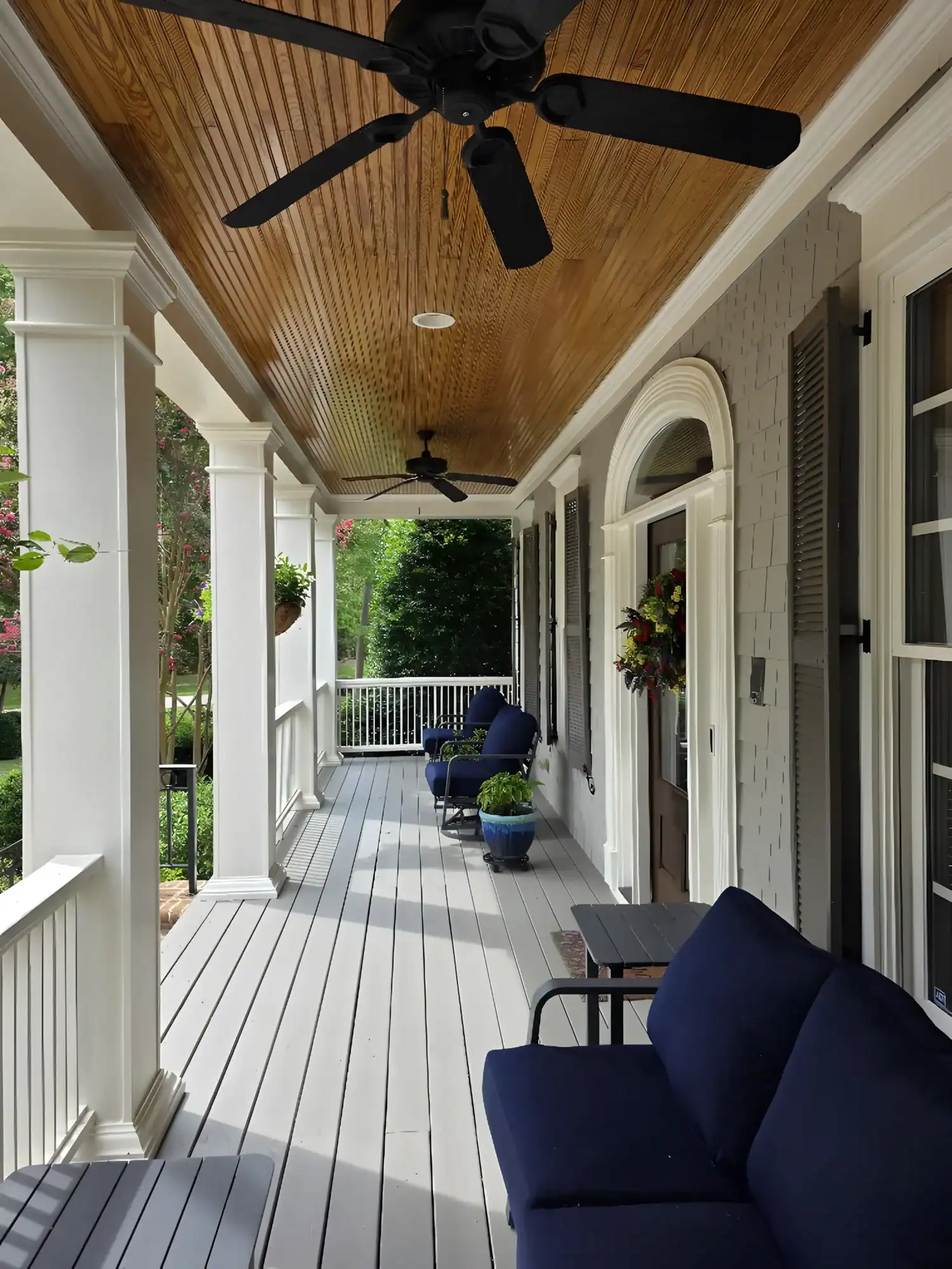 Gray-Painted Residential Deck Gray-painted residential deck with white railings, columns, cedar-shake siding wall, wood ceiling, and black ceiling fans in
