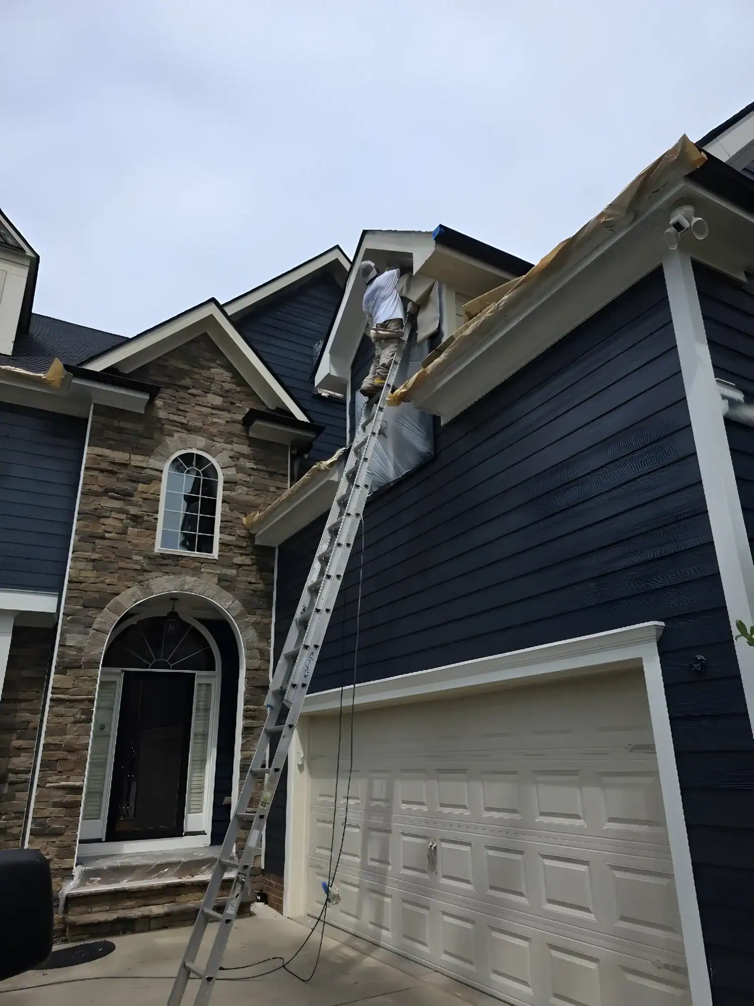Navy Siding Exterior Painting Navy blue horizontal-siding residential home with white trim, brick stone accents, and white garage door in Raleigh, NC