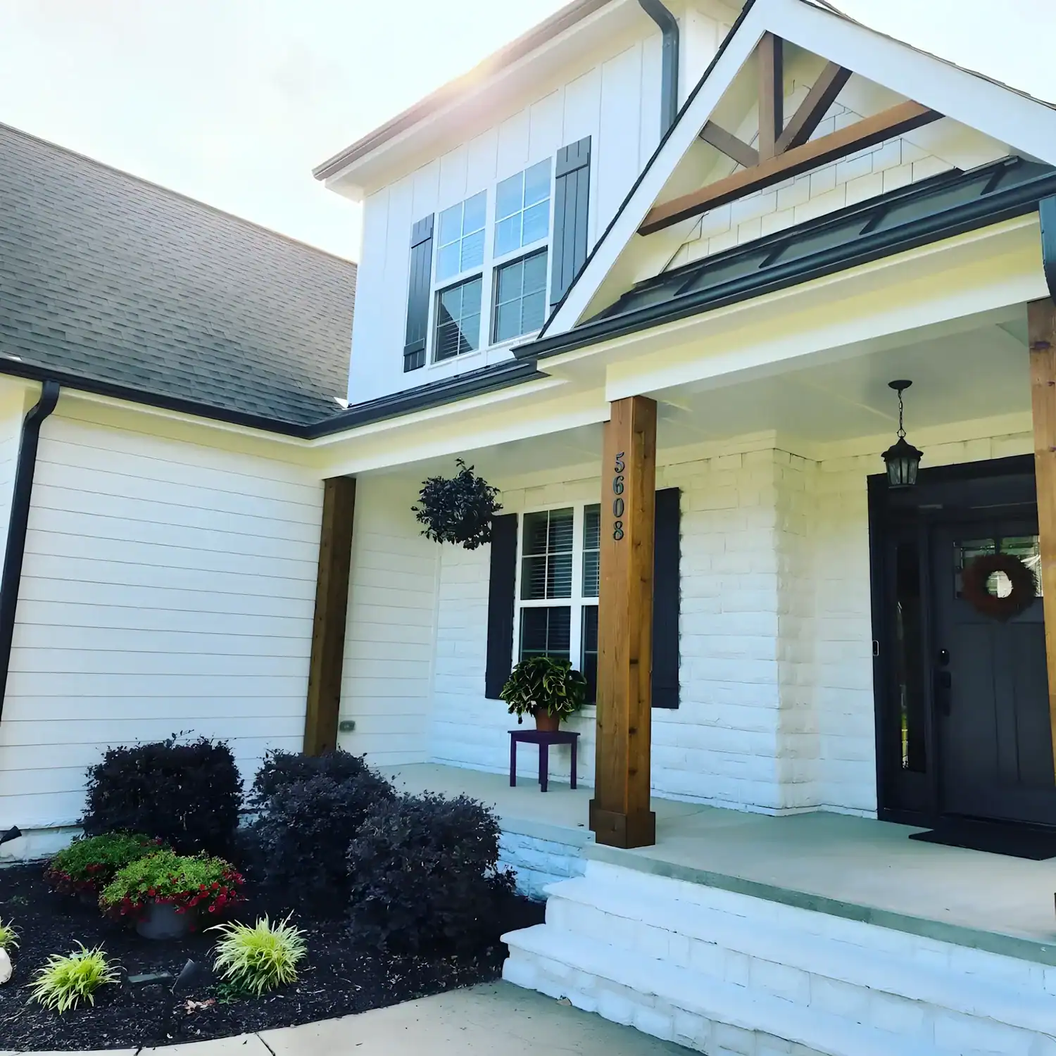White Painted Residential Home Exterior White-painted two-story residential home with black shutters, charcoal roof, wood porch columns, and black entry door in