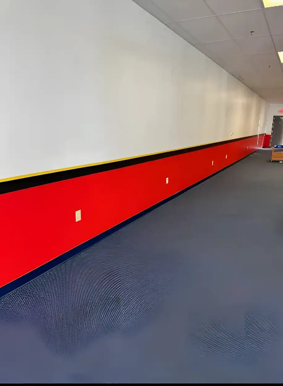 Red And White Painted Commercial Corridor White-painted commercial interior wall with bold red wainscot stripe, yellow and black accent trim, dark blue epoxy floor