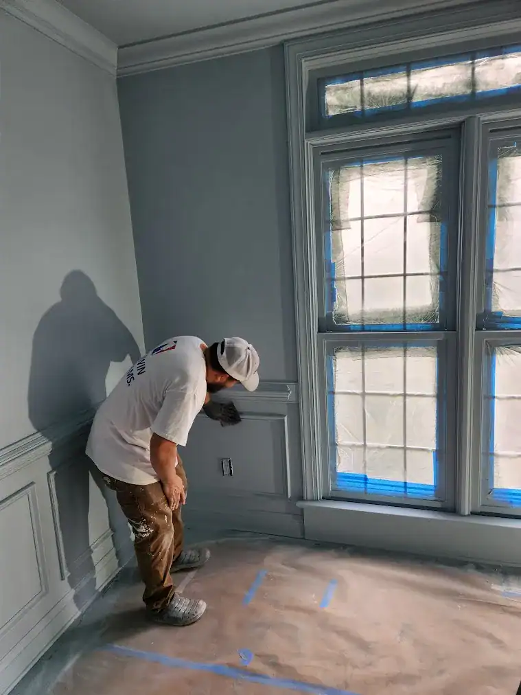 Interior Residential Painting Preparation Painter masking window frame and floor with blue tape during interior residential painting preparation in Raleigh, NC